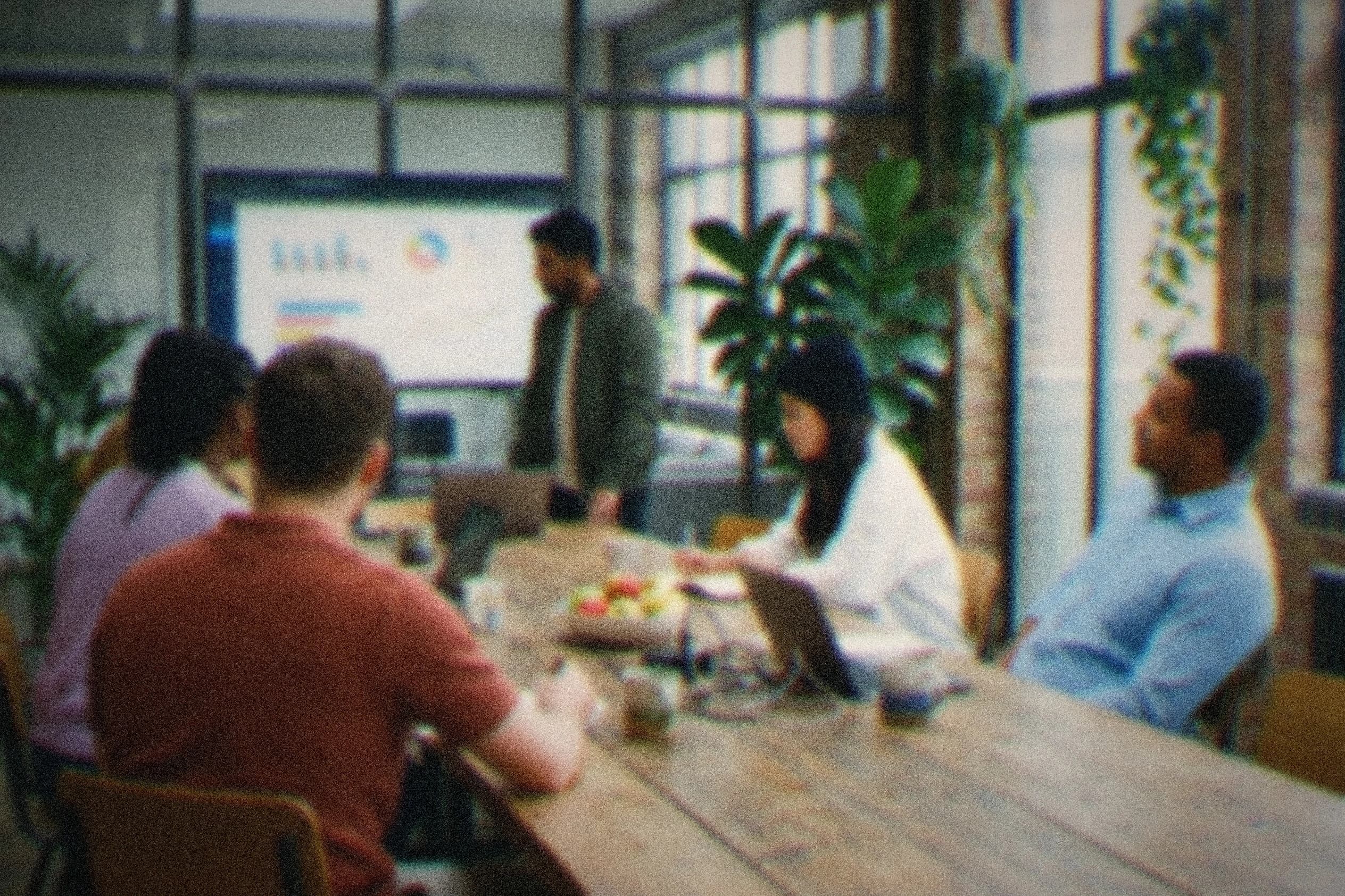 A small cross-functional team around a wooden table, a web app on the wall screen